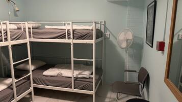 A bunk bed room with a desk, chair, and a standing fan.