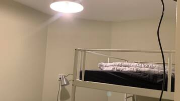 A dormitory room with bunk beds, a desk, and a ceiling light.