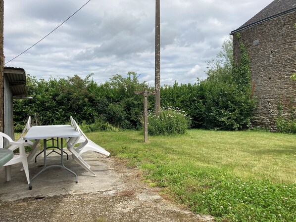 A rustic outdoor area with a concrete table and chairs, surrounded by greenery and a stone wall. - MAGNIFICENT BRETON HOUSE - VIEW OF MONT ST MICHEL - ideal for family reunion. (Sougeal)