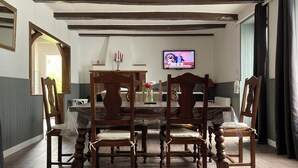 Ein Esszimmer mit Holztisch und -stühlen, einem an der Wand montierten Fernseher und einer Chandelüstere.