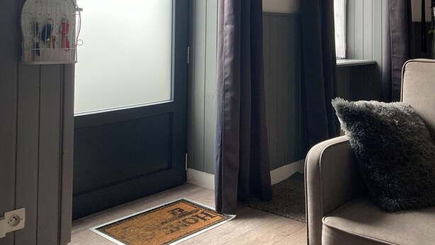 Ein Zimmer mit großem Fenster, einer mit Vorhängen versehenen Tür, einem Sofa mit Kissen, einem kleinen Teppich und einem weißen Vogelkäfig.