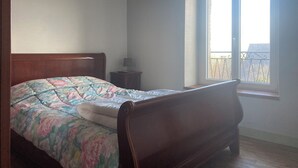 Ein Schlafzimmer mit einem hölzernen Bett, einem Nachttisch und einem Fenster mit Blick auf einen Balkon.