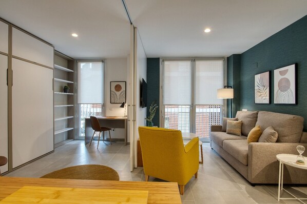 Een moderne woonkamer met een bank, een gele fauteuil, een eettafel en een bureau met stoel.