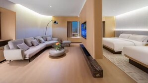 Ein modernes Hotelzimmer mit einer Sitzecke, zwei Betten, einem kleinen Tisch mit Blumen und einem großen Fenster.