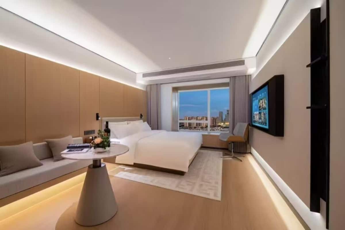 A modern hotel room with a large bed, a sofa, a round coffee table, and a TV mounted on the wall.