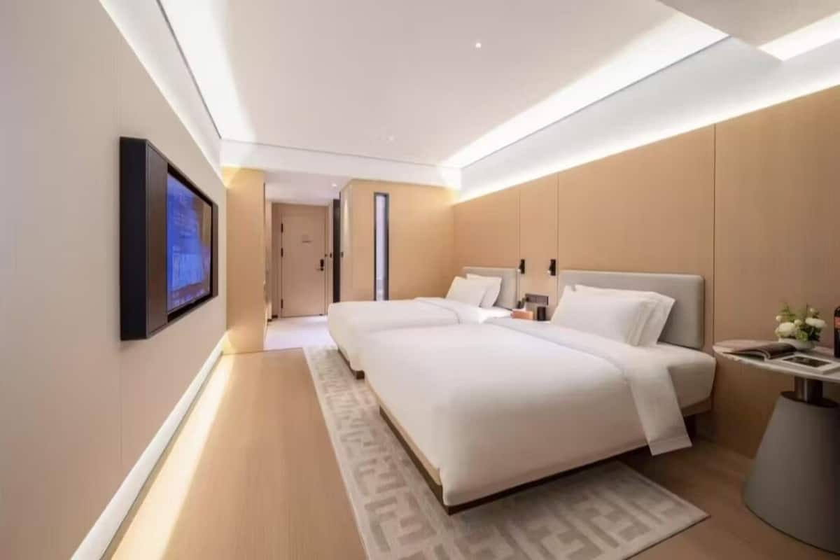 A modern hotel room with a large bed, a bedside table, a flat-screen TV mounted on the wall, and a small side table with a vase of flowers.