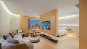 Ein modernes Hotelzimmer mit einer gewölbten Wand, einem großen Flachbildfernseher, einem Sofa, einem Couchtisch und einem Bett.