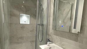 Ein modernes Badezimmer mit einer gläsernen Dusche, einem weißen Waschbecken und einem großen Spiegel.