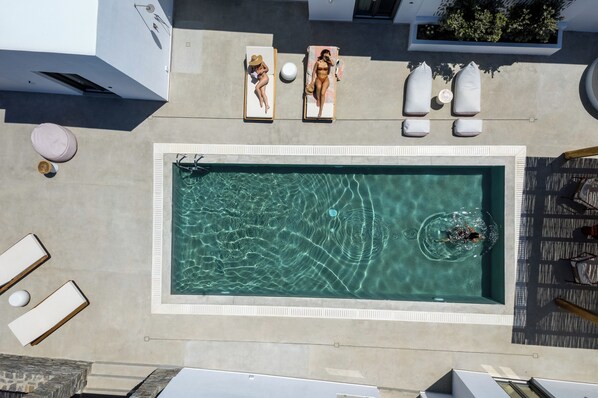 Vue aérienne d’une piscine avec deux chaises longues, une petite table ronde et une zone de terrasse en bois.