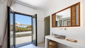 A modern bathroom with a large mirror, a white countertop, and a sliding glass door leading to an outdoor area. - Noble Pearl Villa 3 

Charming 4-bedroom Villa with Swimming pool & Jacuzzi (Paros)