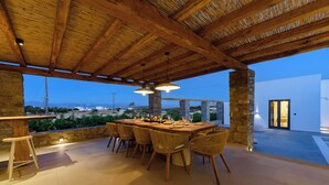An outdoor dining area with a wooden ceiling and stone pillars, featuring a long table and wicker chairs. - Noble Pearl Villa 3 

Charming 4-bedroom Villa with Swimming pool & Jacuzzi (Paros)
