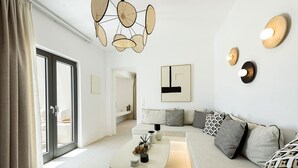 A modern living room with a sofa, a coffee table, and a dining area. There is a large window with curtains, a ceiling light fixture, and wall-mounted decor. - Noble Pearl Villa 3 

Charming 4-bedroom Villa with Swimming pool & Jacuzzi (Paros)