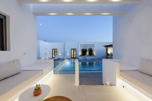 Un espace piscine extérieur moderne, avec des murs blancs et des sièges, offrant une vue dégagée sur le ciel, et agrémenté d’une petite plante en pot posée sur une table.