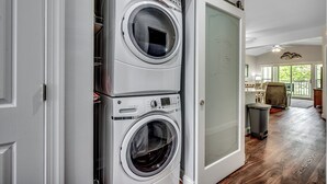 A laundry room with two stacked front-loading washing machines and a glass-enclosed dryer. - Beautiful World Tour 3B3Ba Condo on 12th Hole. Pool Access. Close to Everything! (Myrtle Beach)
