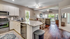 A spacious kitchen with white cabinets, a large island, and a dining area with a view. - Beautiful World Tour 3B3Ba Condo on 12th Hole. Pool Access. Close to Everything! (Myrtle Beach)