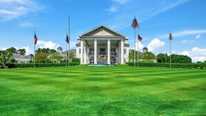 A large, white building with a central entrance and columns, surrounded by a well-maintained lawn and multiple flags. - Beautiful World Tour 3B3Ba Condo on 12th Hole. Pool Access. Close to Everything! (Myrtle Beach)