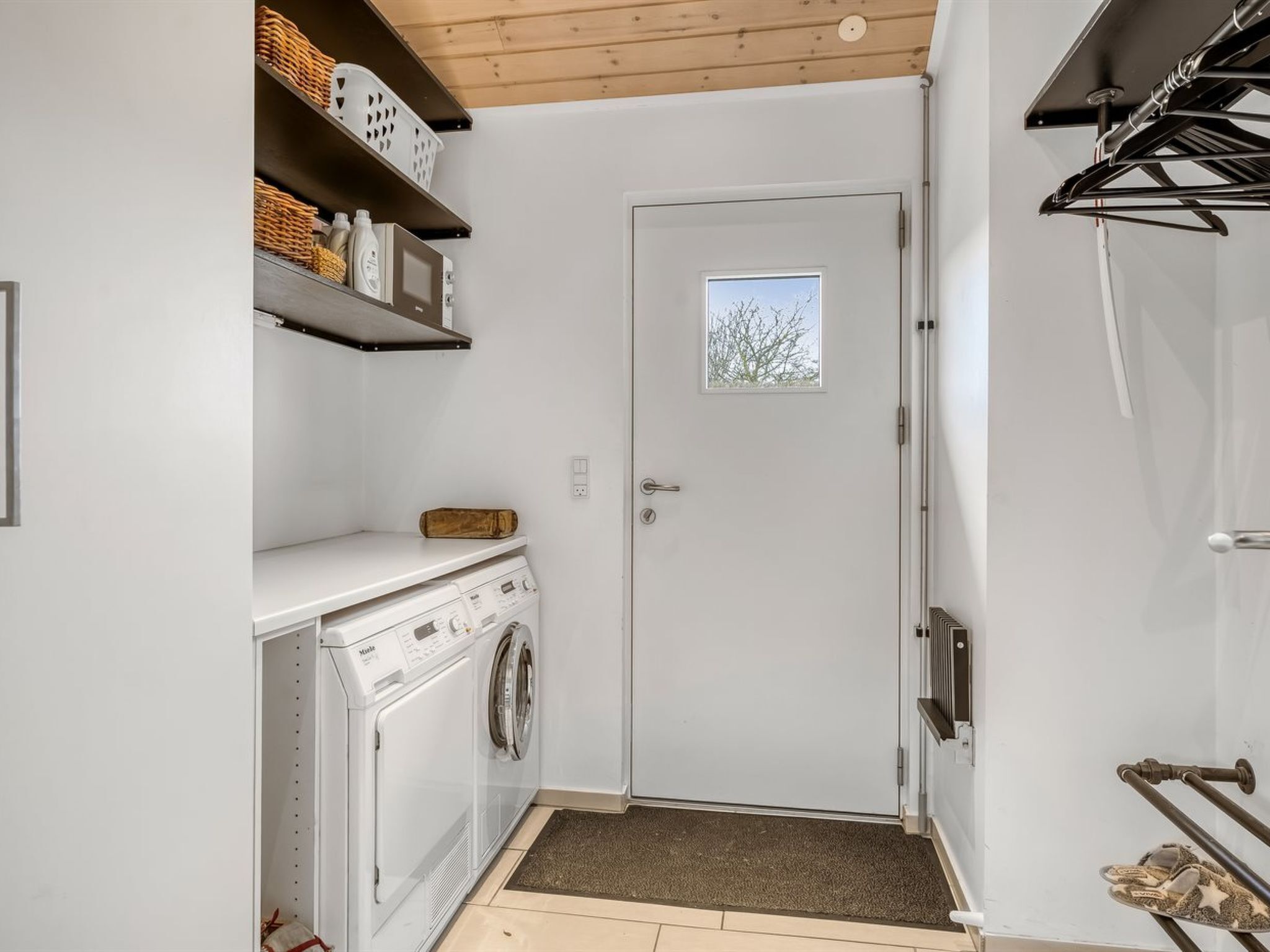 A laundry room with a washing machine, shelves with baskets, and a door with a window.