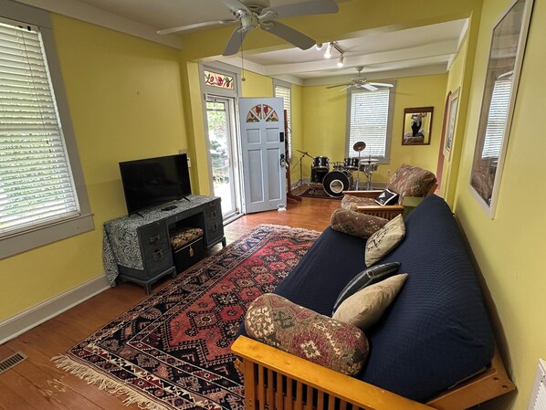 A living room with a sofa, television, patterned rug, and a drum set in the background. - Eastport Bungalow | Yard, Grill & Walk Downtown (Annapolis)