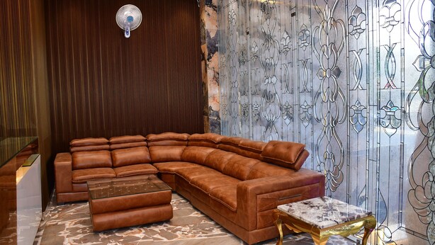 A modern living room with a sectional sofa, a glass coffee table, and a decorative glass partition with floral patterns. - Hotel Blue Stone (Kanpur)
