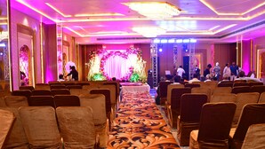 A banquet hall with rows of chairs, a stage with floral decorations, and a chandelier. - Hotel Blue Stone (Kanpur)