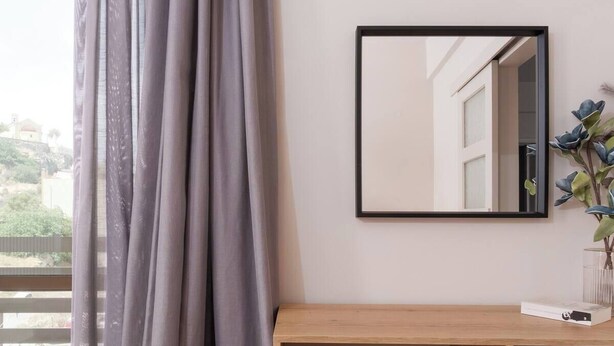 A modern room with a large window, a wooden console table, a mirror, and a small pink ottoman.