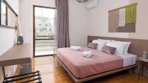 A modern hotel room with a large bed, a desk, and a view through a sliding door to the outside.
