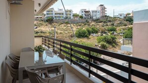 A balcony with a table and chairs, overlooking a hilly residential area with buildings.
