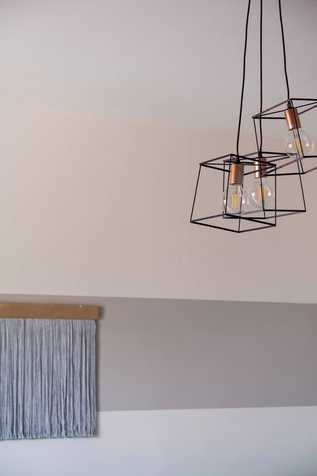A modern ceiling light fixture with three exposed bulbs and copper-colored fixtures, hanging from a geometric metal frame.