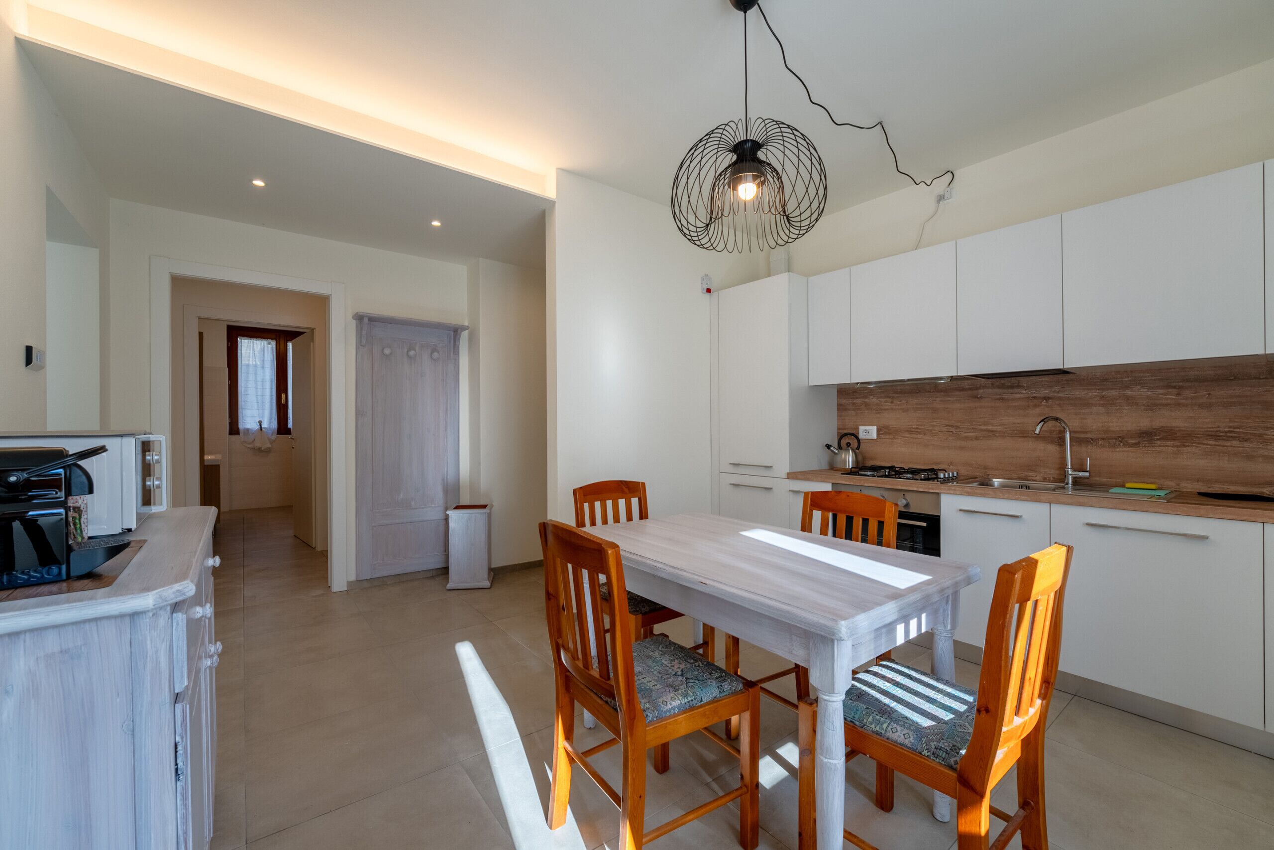 A modern kitchen with white cabinets, a wooden countertop, and a dining area with a white table and wooden chairs.