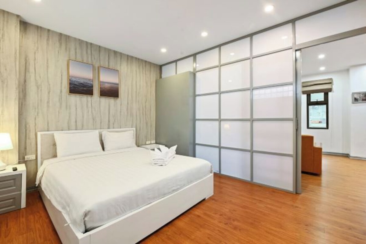 Ein modernes Hotelzimmer mit einem großen Bett, Holzboden, einer Schiebeglastür und einem Schreibtisch mit Lampe.