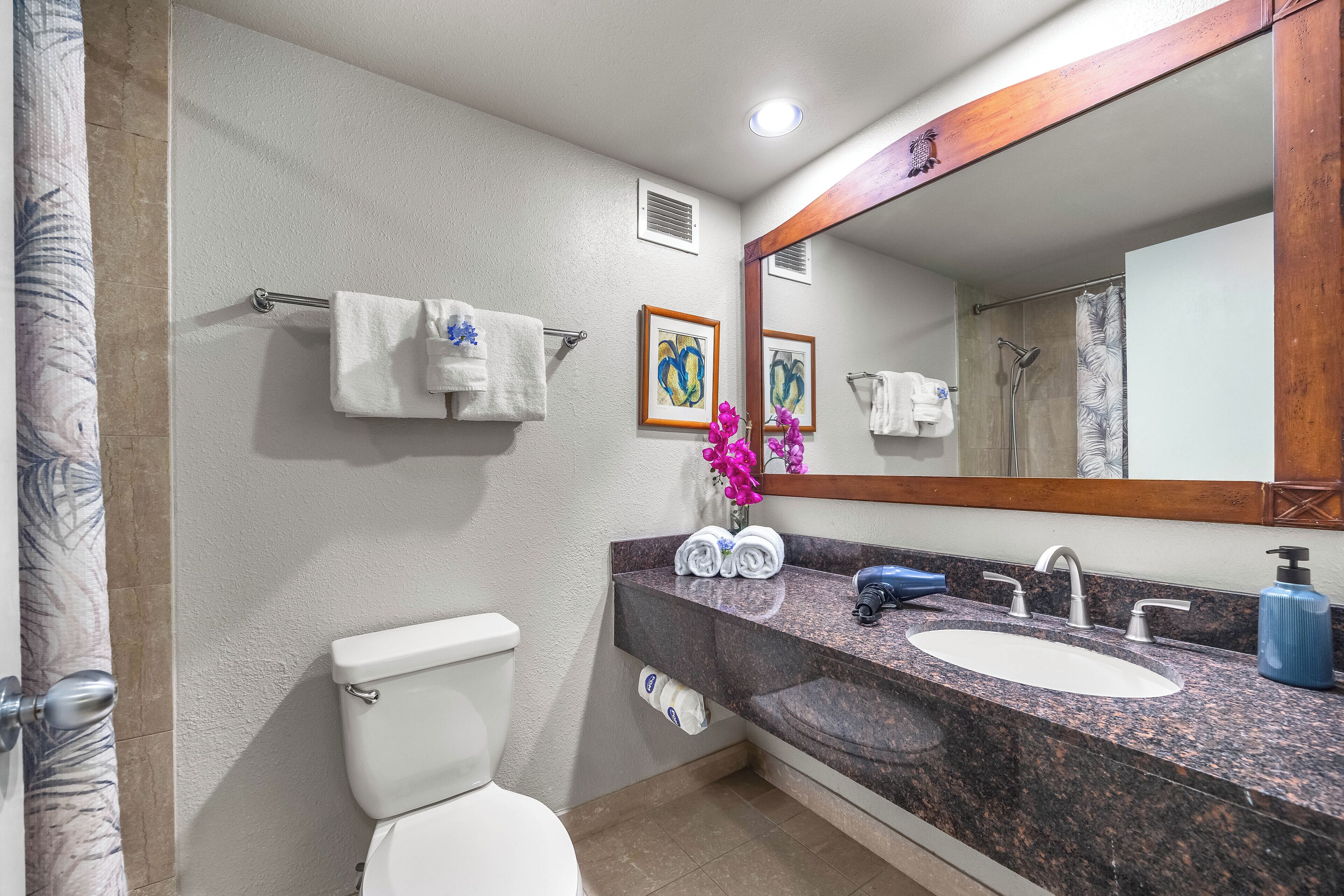A bathroom with a toilet, sink, and shower. There are towels and a mirror.