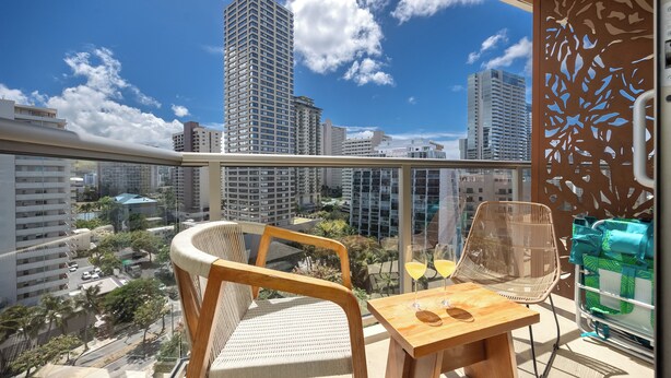Un balcon avec deux fauteuils en osier, une petite table en bois et une cloison en verre ornée d’un motif décoratif.