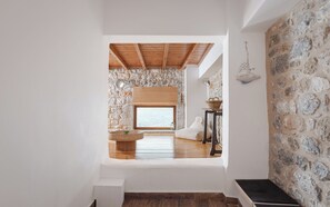 Un'ampia stanza con parete in pietra, soffitto in legno e una grande finestra con vista su un corpo d'acqua.
