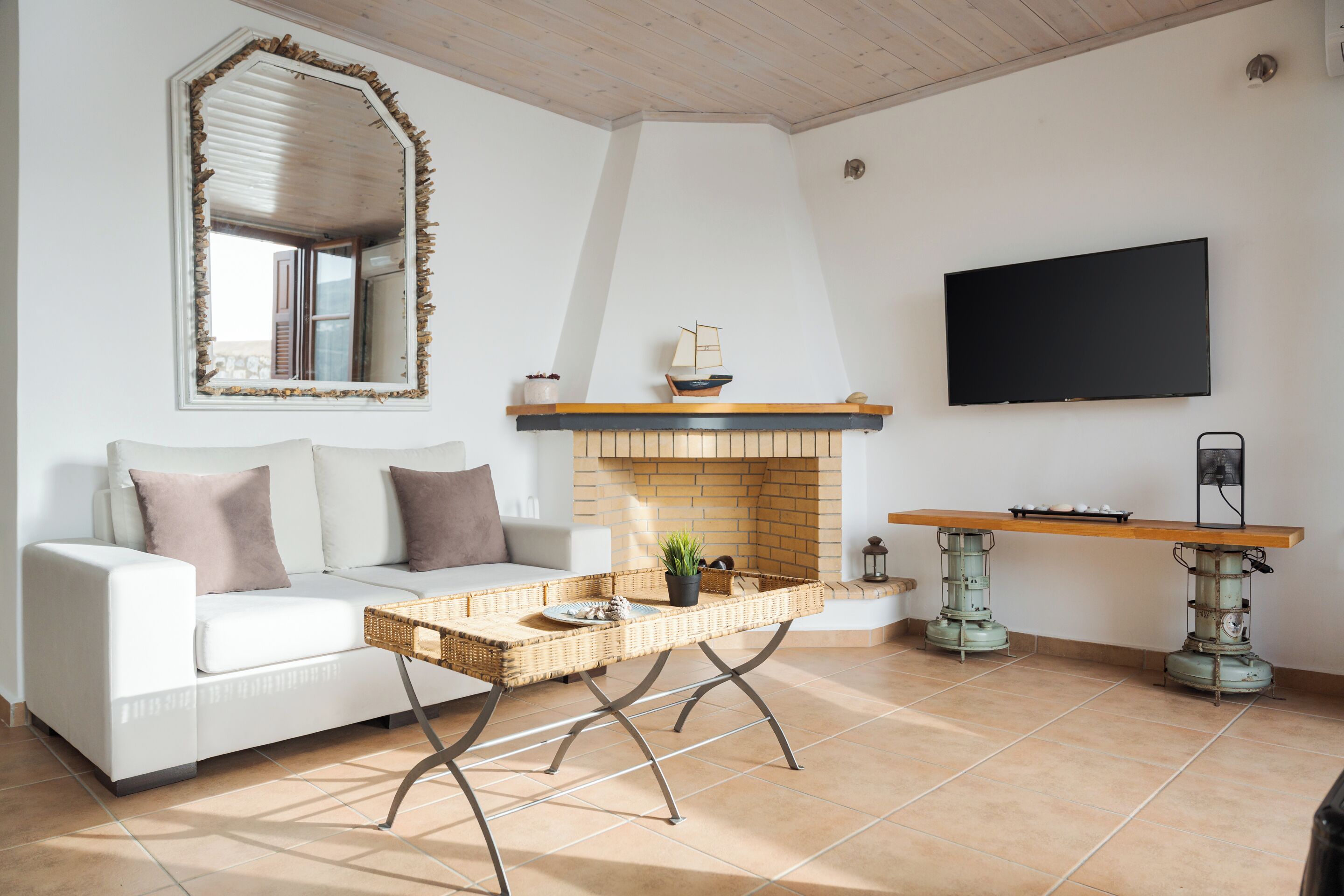 A living room with a white sofa, a wicker coffee table, a fireplace, and a flat-screen TV mounted on the wall.