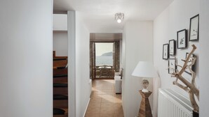 A hallway leading to a dining area with a view of the sea, a staircase, and a wall with framed pictures. - Aura Seafront Villa (Neo Itilo)