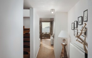 Un corridoio che conduce a una zona pranzo con vista sul mare, una scala e una parete con quadri appesi.