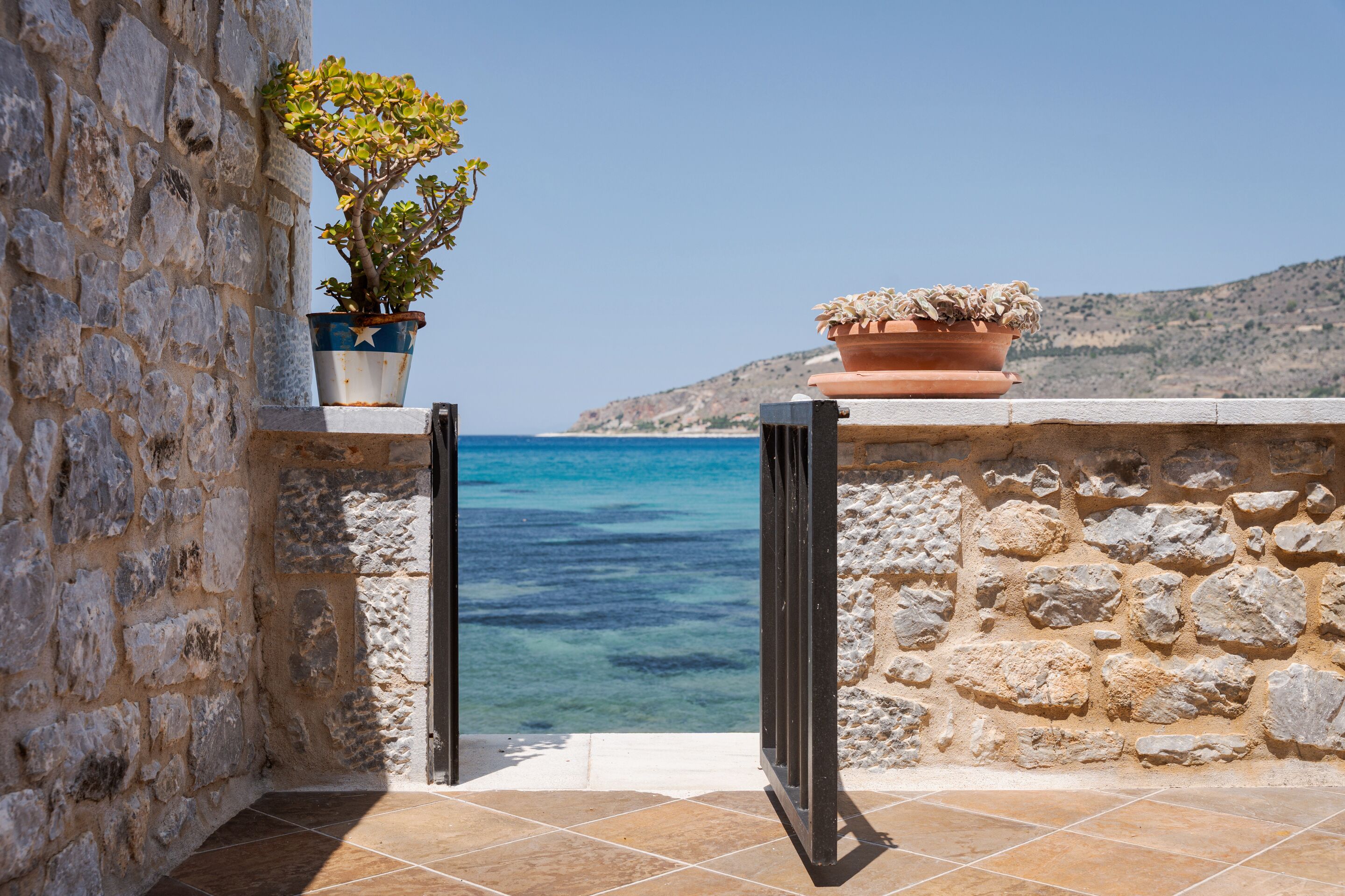A stone wall with a potted plant and a view of the sea.