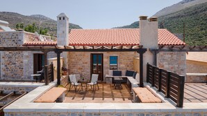 A stone building with a tiled roof, outdoor seating area, and a view of the mountains. - Aura Seafront Villa (Neo Itilo)