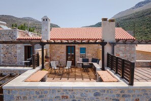 A stone building with a tiled roof, outdoor seating area, and a view of the mountains. - Aura Seafront Villa (Neo Itilo)