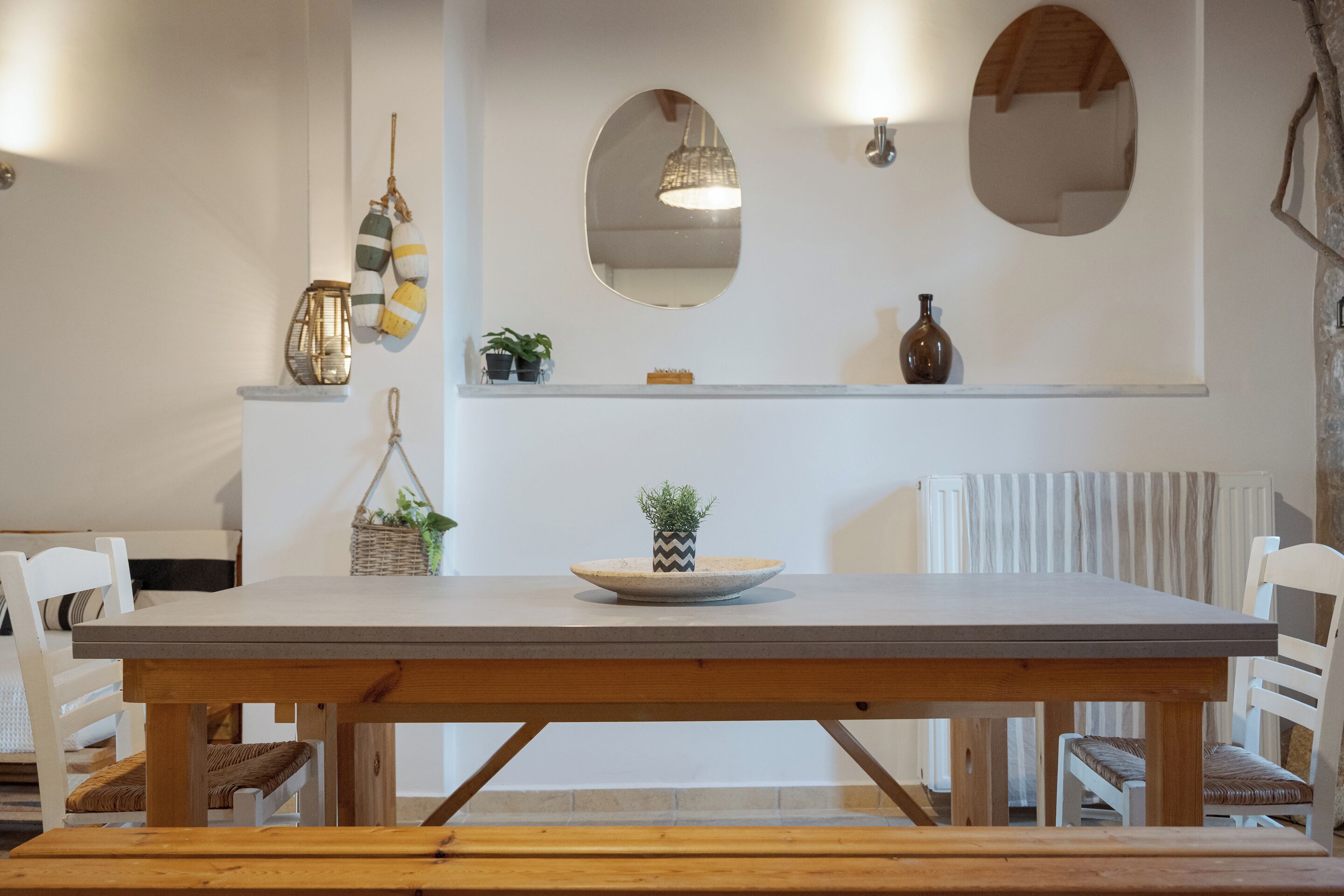 Un comedor con una mesa de madera, sillas blancas, una lámpara colgante y un espejo en la pared.