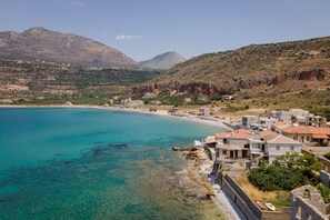 A coastal town with clear turquoise waters, a sandy beach, and buildings with red-tiled roofs. - Aura Seafront Villa (Neo Itilo)