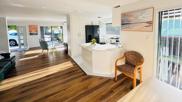A modern kitchen with white cabinets, a central island, and a dining area with a wooden floor.