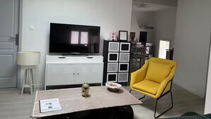 Un salon avec un téléviseur à écran plat, une petite statue de Bouddha, un fauteuil jaune et un meuble décoratif.