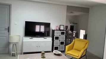 Un salon avec un téléviseur à écran plat, une petite statue de Bouddha, un fauteuil jaune et un meuble décoratif.