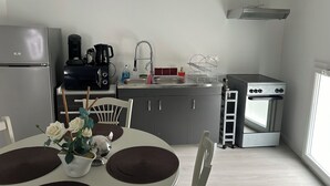 Une cuisine compacte équipée d’un réfrigérateur, d’une machine à café, d’un évier, d’une cuisinière et d’un coin repas avec une table et des chaises.