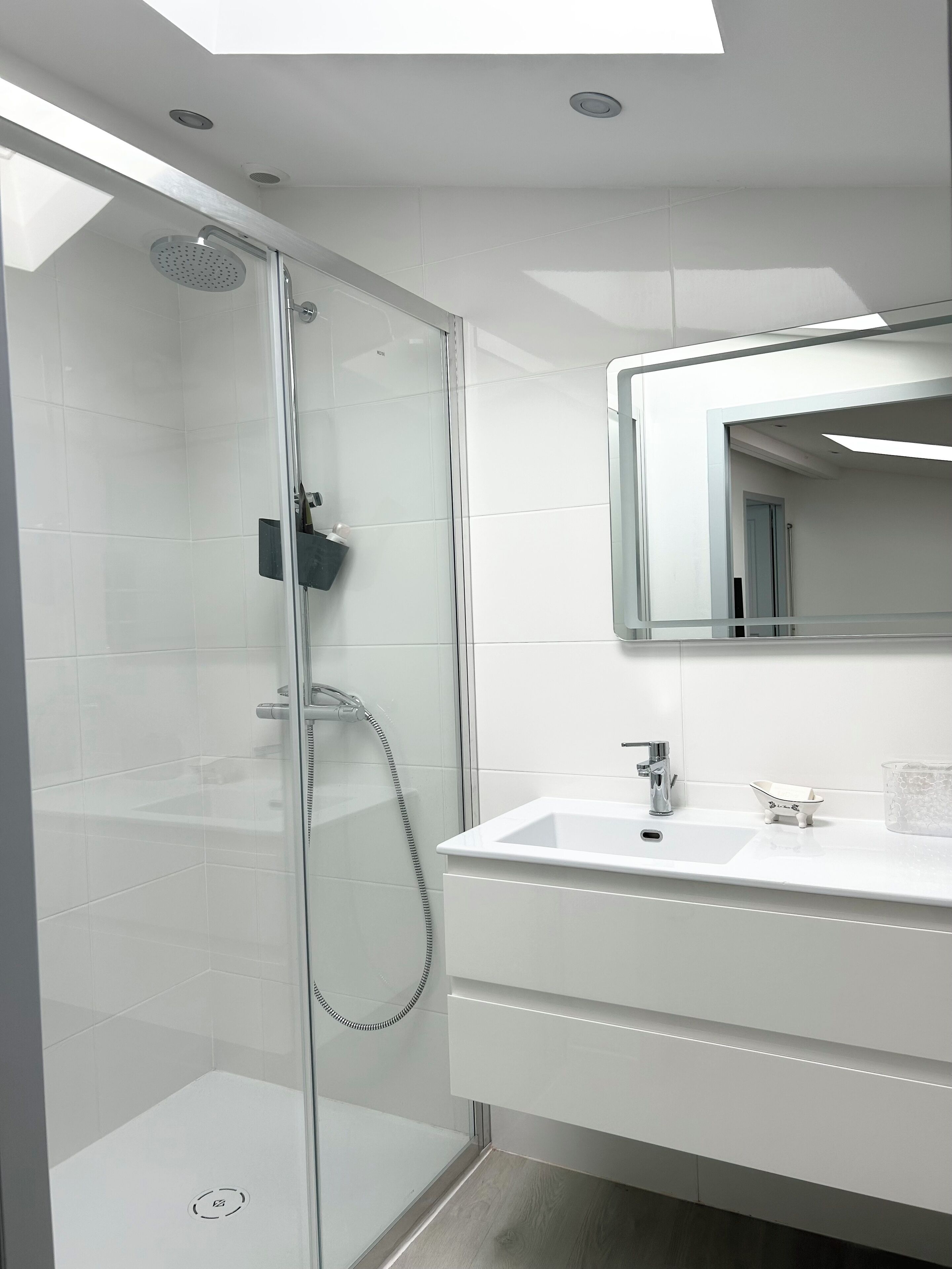 Une salle de bain moderne avec une douche à parois de verre, un lavabo blanc avec un miroir et une petite baignoire.