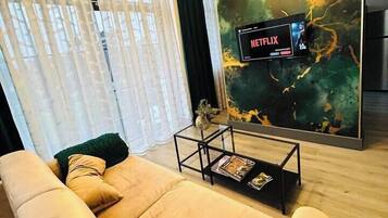 Un salon moderne avec un canapé beige, une table basse en verre et un grand tableau abstrait accroché au mur.