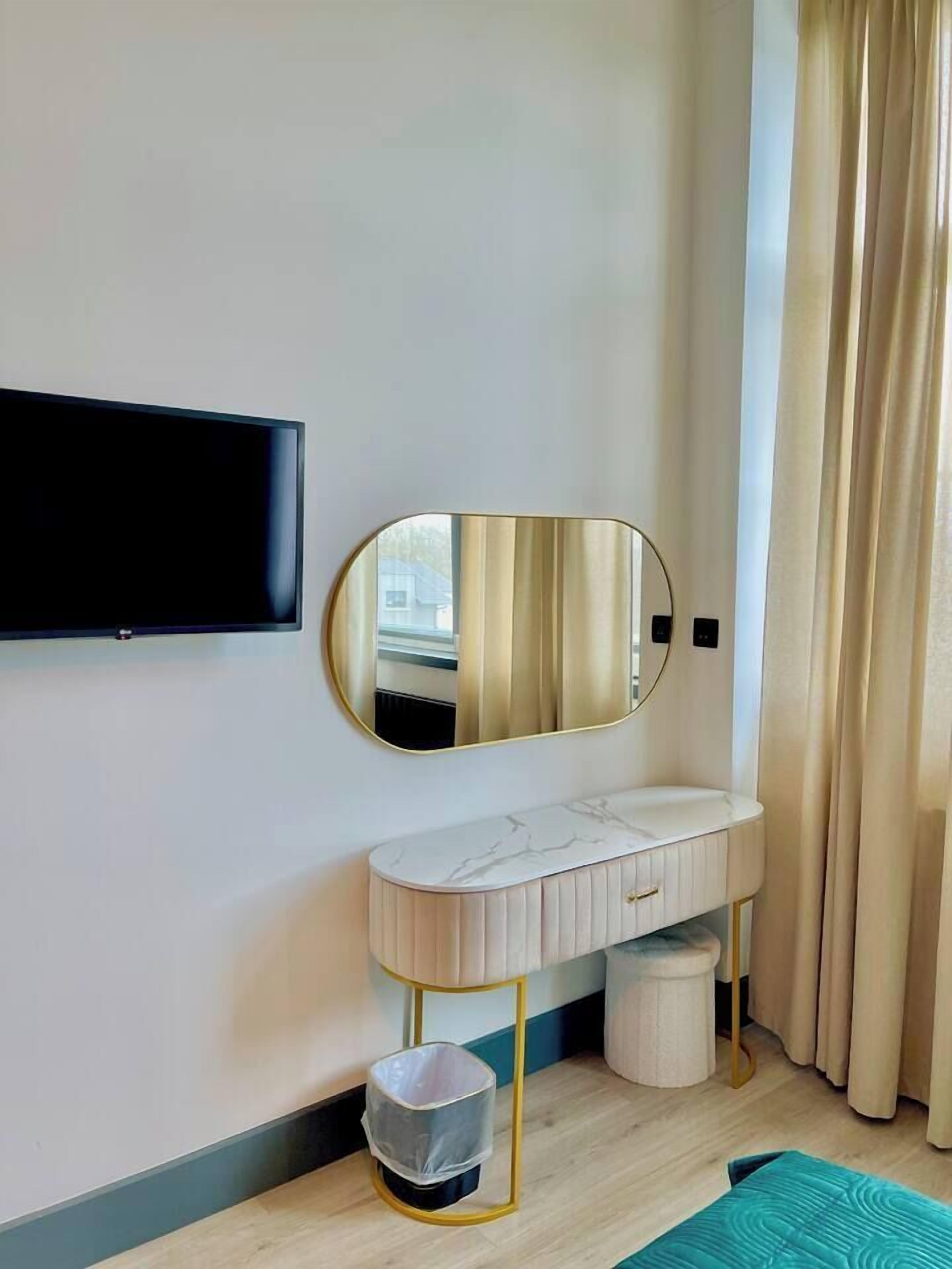 Un bany modern amb televisió penjada, un lavabo amb taulell de marbre, un mirall amb marc daurat i un petit cendrer.
