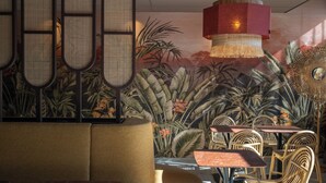 L’intérieur d’un restaurant est décoré d’une fresque aux motifs tropicaux, de meubles en osier et d’un luminaire rouge suspendu.