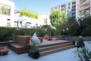 An outdoor patio area with wooden seating, potted plants, and a view of surrounding buildings. - Hotel Oceania Lyon (Lyon)